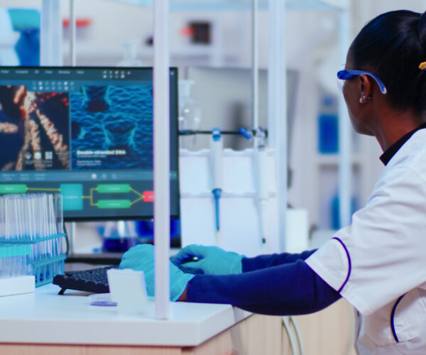 African woman biochemist researcher checking manifestations of vaccine working in modern equipped laboratory. Multiethnic doctors examining virus evolution using high tech researching diagnosis
